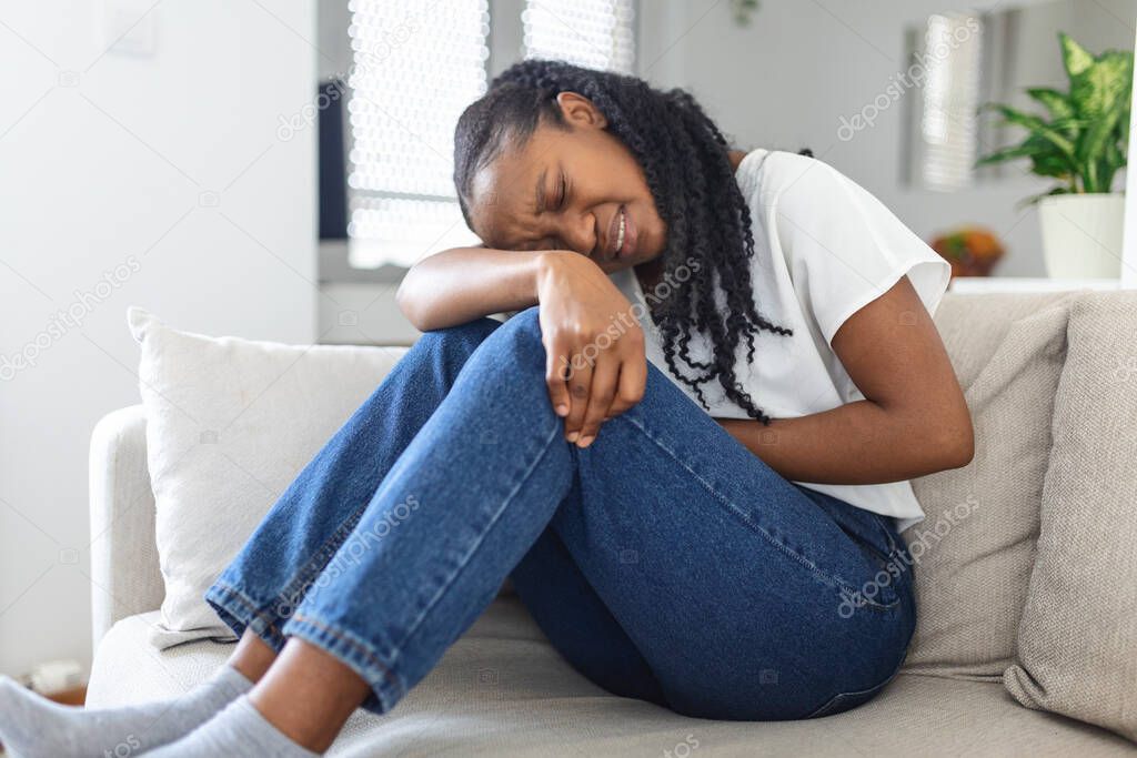 Woman in painful expression holding hands against belly suffering menstrual period pain, lying sad on home bed, having tummy cramp in female health concept