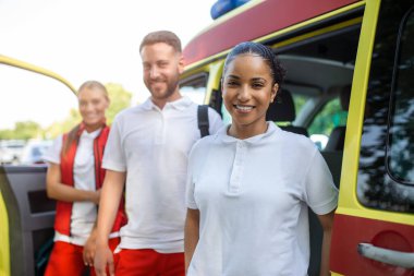 Ambulansın yanında bekleyen çok ırklı sağlık görevlileri var. Acil servis doktorları ve hemşire ambulansın önünde duruyor.