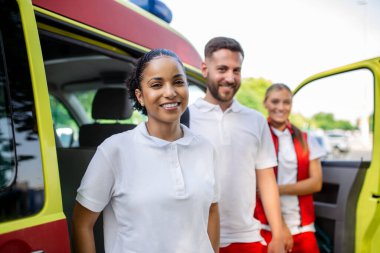 Ambulansın yanında bekleyen çok ırklı sağlık görevlileri var. Acil servis doktorları ve hemşire ambulansın önünde duruyor.