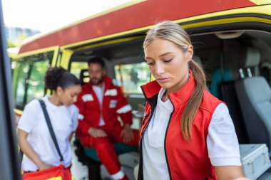 Ambulans aracının önünde portatif ekipman taşıyan üç çok ırklı sağlık görevlisi.