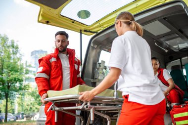 Ambulansın yanında sedye taşıyan sağlık görevlileri. Sağlık görevlileri ambulans arabasını sedyeyle çıkarıyorlar.
