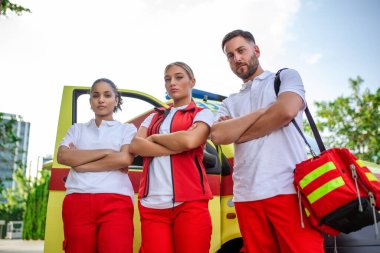 Ambulansın yanında bekleyen çok ırklı sağlık görevlileri var. Acil servis doktoru ve hemşire ambulansın önünde duruyor.
