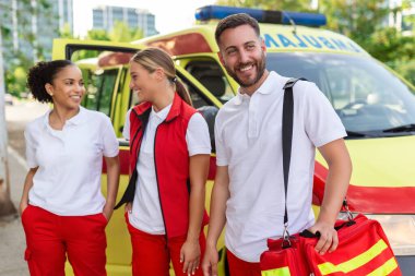 Ambulansın yanında bekleyen çok ırklı sağlık görevlileri var. Acil servis doktoru ve hemşire ambulansın önünde duruyor.