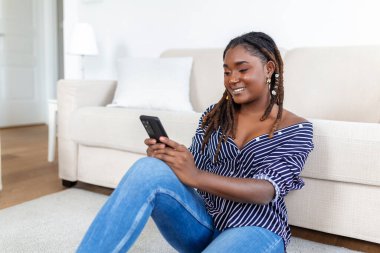 Evdeki kanepede dinlenirken cep telefonu kullanan genç bir kadının fotoğrafı.