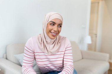 Kendine güvenen, tesettürlü, gülümseyen ve kameraya bakan Orta Doğulu genç bir kadının portresi.