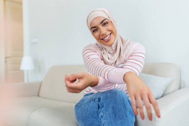 Kendine güvenen, tesettürlü, gülümseyen ve kameraya bakan Orta Doğulu genç bir kadının portresi.