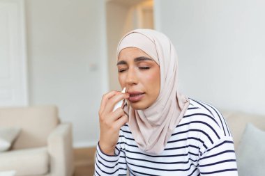 Güzel, genç, Arap bir kadının burun deliğini tıkayan burun spreyi koklaması portresi. Burun tıkanıklığı için burun tıbbı kullanmaktan hasta olan kadının yakınlaşması..