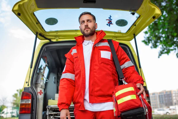 Ambulance staff member emerges from the back of an ambulance with his emergency backpack , and vital signs monitor .