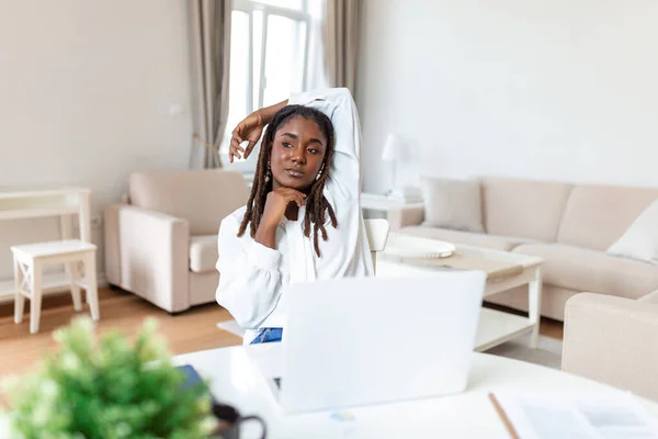 Pretty African lady with black hair working at laptop sitting at a table at home - check out online stores selling cyber mondays - tech woman concept for alternative freelance office