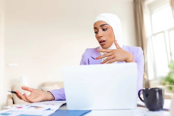 Muslim woman working with computer. Arab Young business woman sitting at her desk at home, working on a laptop computer and drinking coffee or tea. Muslim woman working at a home and using computer.