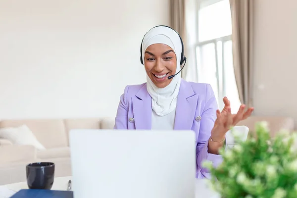 Businesswoman in hijab having a video chat on laptop . Female sitting at cafe and making video call using earphones and laptop computer.