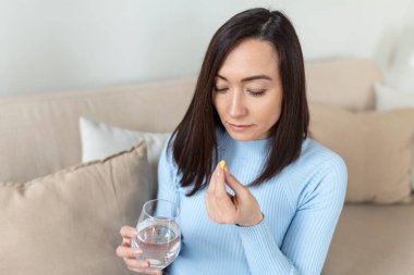 Asyalı kadın elinde bir bardak suyla hap alıyor. Stresli kadın antidepresan ilaçlar içiyor. Kadın depresyonda, uyuşturucu kullanıyor. İşteki ilaçlar