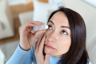 Göz damlası kullanan bir kadın, göz veya alerji tedavisi için göz kremi kullanan bir kadın, göz tahrişi ya da iltihaplı kadın, optik semptomlar.