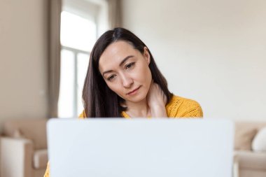 Bitkin hissediyorum. Hüsrana uğramış Asyalı kadın yorgun görünüyor ve iş yerinde otururken boynuna masaj yapıyor.