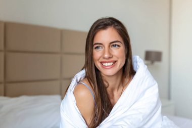 Uyandıktan sonra battaniyeye sarılmış bir kadın, iyi bir uykudan sonra bir güne mutlu ve rahat giriyor. Tatlı rüyalar, günaydın, yeni gün, hafta sonu, tatil konsepti