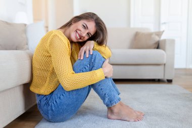 Yerde oturan ve kameraya bakan mutlu genç kadın. Kışlık giysiler içinde rahat bir kadın portresi koltukta dinleniyor. Güz boyunca gülümseyen ve rahatlatan güzel bir kadının portresi..