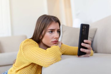 Dalgın, üzgün, genç bir kadın elinde akıllı telefonuyla mesaj bekliyor ya da erkek arkadaşından telefon bekliyor..