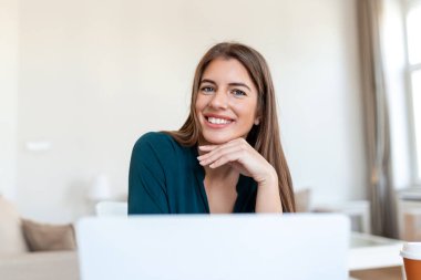 Evden bilgisayarda çalışan bir kadın, kameraya bakan güzel bir kadının portresi.