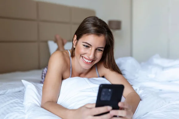 Donna Sorridente Guardando Telefono Cellulare Mentre Giaceva Sul Letto Bianco — Foto Stock