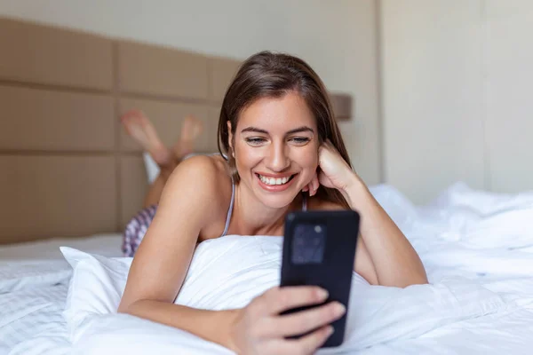 Donna Sorridente Guardando Telefono Cellulare Mentre Giaceva Sul Letto Bianco — Foto Stock