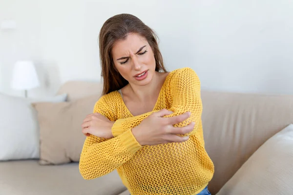 Blond woman with arm pain. Female massaging painful hand indoors. Young woman hand holding her elbow suffering from elbow pain. pain in hand at home, health