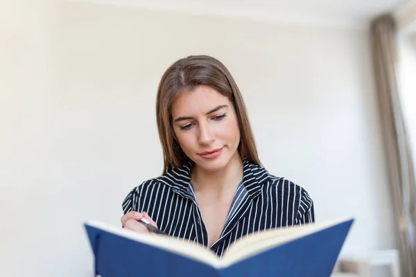 Young beautiful woman holding book, University student studying, learning language. leisure, literature and people concept - smiling woman reading book at home