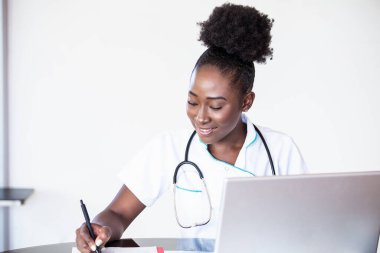 Hastanede çalışan bir doktor reçete, sağlık sigortası ve tıbbi konsept yazıyor, test sonuçları arka planda, stetoskop ve masaüstü bilgisayarı olan