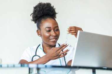 Female doctor in white coat holding blood test tubes in hands while wrapped up in work at modern lab. Female life science professional holding glass cuvette. Healthcare and biotechnology concept.