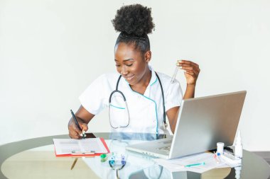 Female doctor in white coat holding blood test tubes in hands while wrapped up in work at modern lab. Female life science professional holding glass cuvette. Healthcare and biotechnology concept.