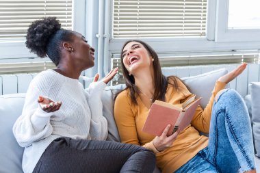 Evdeki kitaplardan komik hikayelere gülen iki kadın. Arkadaşlık ve bakım, mutlu kız arkadaşlar. Afro-Amerikalı ve Kafkasyalı en iyi arkadaşlar evde eğleniyor, gülüyor ve komik bir kitap okuyor..