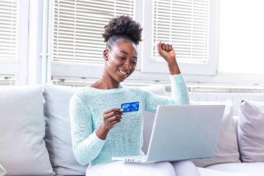 Genç ve güzel bir kadın internetten alışveriş malzemeleri bulduğu için mutlu. Güzel kız evde online alışveriş için dizüstü bilgisayar kullanıyor.