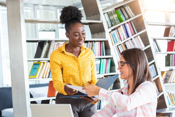 Рабочая группа беседует за столом с ноутбуком в современном офисе. Два человека обсуждают информацию, увиденную на экране серебристого устройства, и дружелюбно улыбаются. Перспективный персонал, одетый в формальную одежду