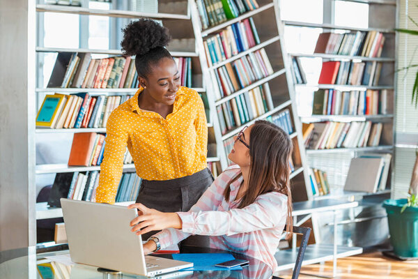Двое коллег по бизнесу рассматривают ноутбук и обсуждают свой стартап-план в современном офисе. Афроамериканская деловая женщина и ее партнер сидят за столом и обсуждают будущие сделки