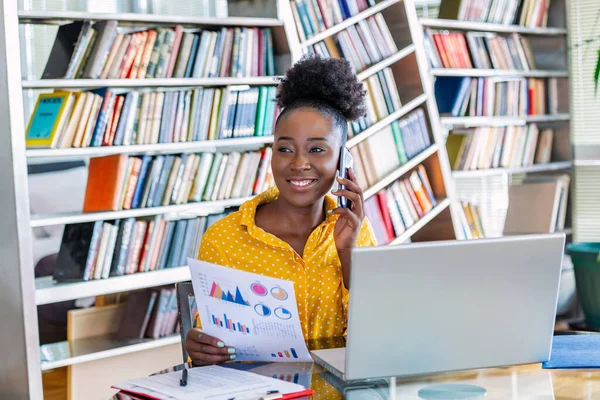 Female businessmen in casual wear work at the desk about accounting and business plan analysis. Young black woman talking on phone at her desk in an office.