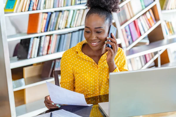 Attractive businesswoman, speaking on the phone, African American woman at training seminar, female business leader going true paperwork at her office