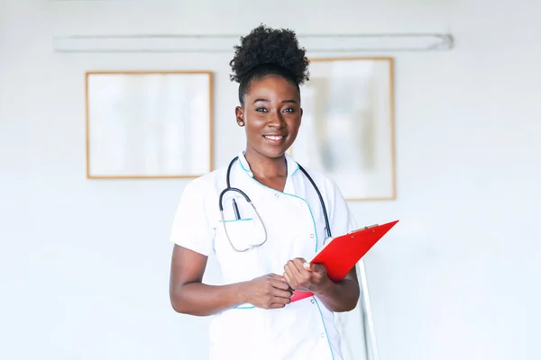 Confident smiling doctor posing and looking at camera with clipboard in her hands. Friendly African American female doctor smiling. Doctor with stethoscope around her neck