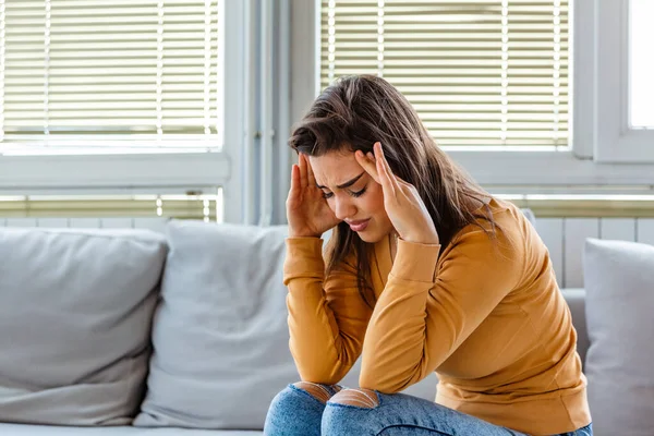 Evdeki kanepede baş ağrısı ve sırt ağrısıyla oturan esmer bir kızın portresi. Kronik günlük baş ağrısı çeken güzel bir kadın. Sinüs ağrısı yüzünden kafasını tutan üzgün bir kadın.