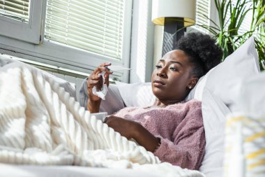 Hastalık, mevsimsel virüs problemi konsepti. Kanepede uzanmış, termometredeki sıcaklığa bakarak hasta olan bir kadın. Hasta kadın yüksek ateşle yatakta yatıyor. Soğuk algınlığı ve migren.
