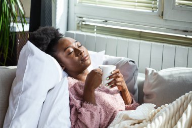 Hasta olduğu için evde. Afro-Amerikalı kadının burnu akıyor ve nezle olmuş. Öksür. Soğuk algınlığına ya da gribe yakalanmış güzel genç bir kadının yakın çekimi. Boğazında Ağrı Olan Sağlıksız Kızın Portresi.