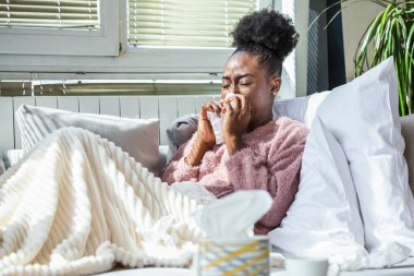 Battaniyenin altında oturan hasta Afrikalı Amerikalı kadın. Yatağında battaniyeyle yatan hasta kadın mevsimsel enfeksiyonlar, grip, alerji....