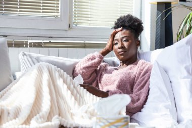 Soğuk ve soğuk algınlığı. Hasta ve başı ağrıyan Afrika kökenli Amerikalı bir kadının portresi. Battaniyeye sarılı güzel, sağlıksız kızın acı dolu kafasını sağlık sigortası kavramına yakın çekim..