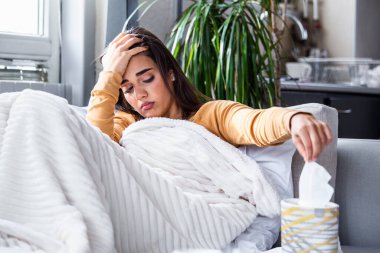 Sickness, seasonal virus problem concept. Woman being sick having flu lying on sofa. Sick woman lying in bed with high fever. Cold flu and migraine.