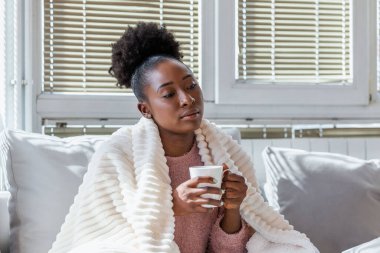 Hasta olduğu için evde. Afro-Amerikalı kadının burnu akıyor ve nezle olmuş. Öksür. Soğuk algınlığına ya da gribe yakalanmış güzel genç bir kadının yakın çekimi. Çay İçen Sağlıksız Kızın Portresi.
