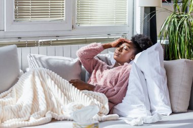 Hasta kadın. Flu. kadın üşüttü. Dokuların içine hapşırmak. Baş ağrısı. Virüs. İlaçlar. Burnunu mendile sümküren soğuk algınlığına yakalanmış genç bir kadın. Kanepede oturan, başı ağrıyan hasta kadın.