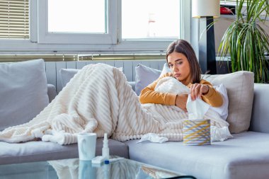 Hasta kadın. Flu. kadın üşüttü. Dokuların içine hapşırmak. Baş ağrısı. Virüs. İlaçlar. Burnunu mendile sümküren soğuk algınlığına yakalanmış genç bir kadın. Kanepede oturan, başı ağrıyan hasta kadın.