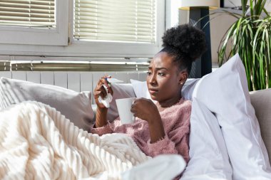 Hastalık, mevsimsel virüs problemi konsepti. Kanepede uzanmış, termometredeki sıcaklığa bakarak hasta olan bir kadın. Hasta kadın yüksek ateşle yatakta yatıyor. Soğuk algınlığı ve migren.