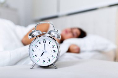 Wake up of an asleep girl stopping alarm clock on the bed in the morning. woman sleeping and wake up to turn off the alarm clock in the morning