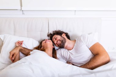 Mutlu çift yatakta birlikte yatıyor. Birbirinin dostluğunun keyfini çıkarıyorum. Mutlu genç bir çift evdeki yatak odasında yatarken sarılıyor ve gülümsüyor..