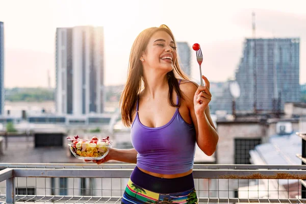 Young caucasian woman eating salad outdoor in sunset. Healthy Diet. Beautiful Smiling Woman Eating Fresh Organic Vegetarian Salad. Healthy Eating, Food And Lifestyle Concept. Health, Beauty