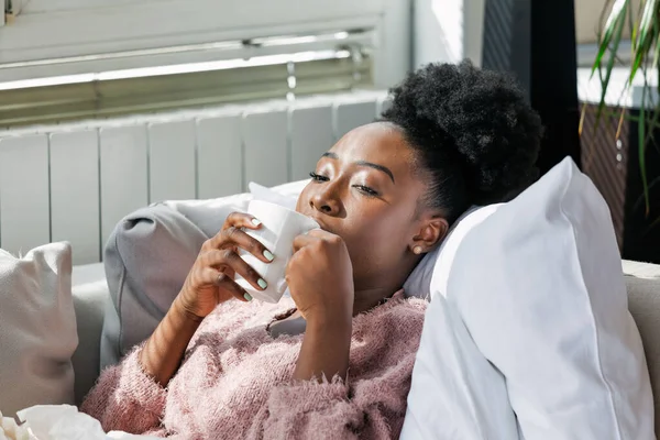 Sick desperate woman has flu. Rhinitis, cold, sickness, allergy concept. Pretty sick woman has runnning nose, rubs nose with handkerchief. African American woman Sneezing in a tissue